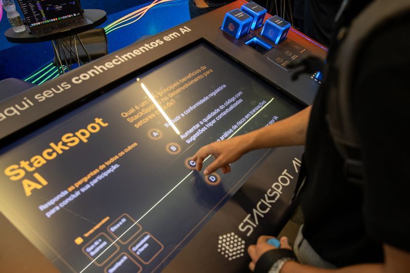 Imagem de uma das ativações levadas pela Zup para o evento. Nela há uma pessoa clicando em uma tela, jogando um jogo de perguntas e respostas sobre os benefícios da StackSpot. 