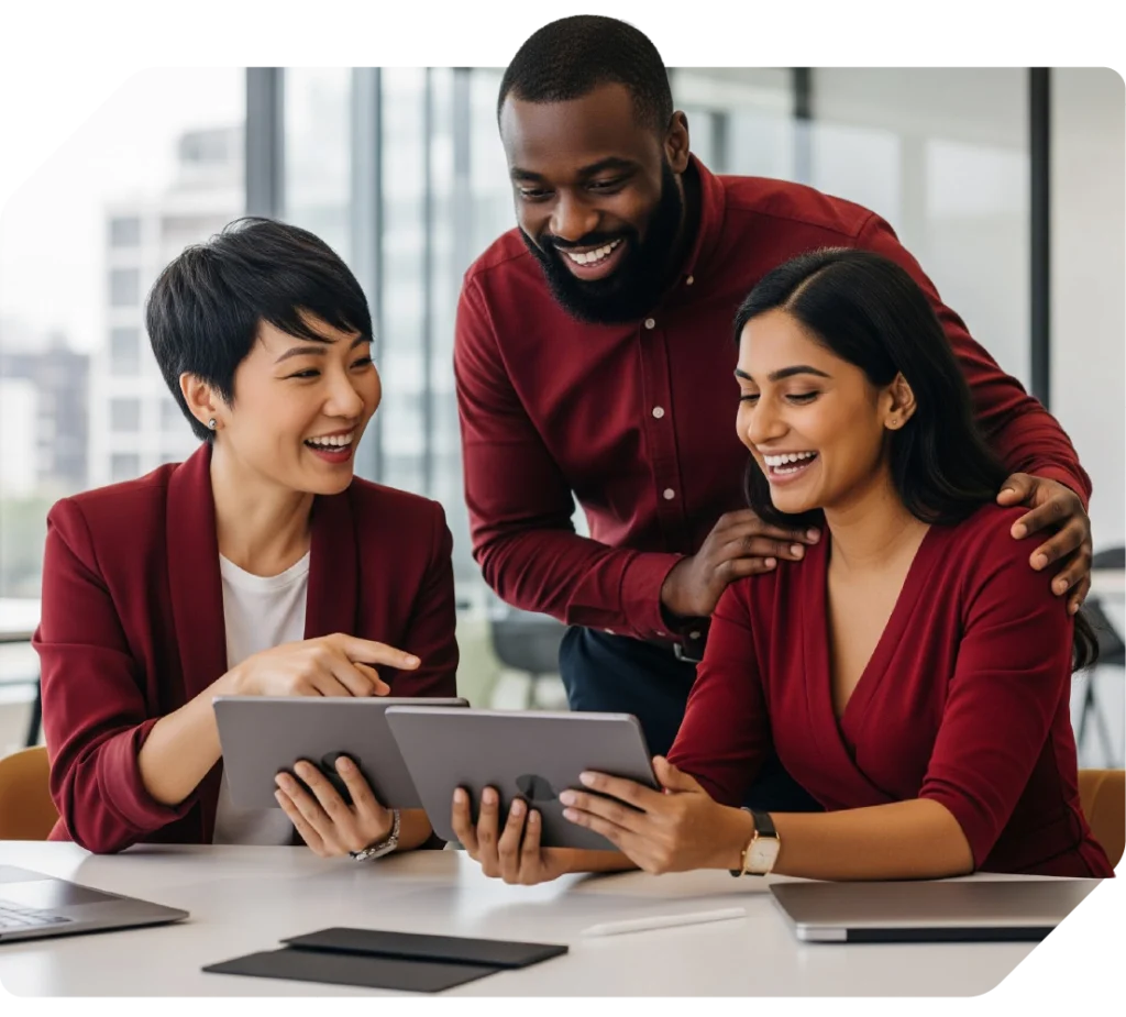 Equipe diversa de três profissionais em escritório: mulher asiática de pele clara com cabelo curto usando blazer vermelho, homem negro com barba usando camisa vinho e mulher de pele morena com cabelo longo usando blazer vermelho, todos sorrindo enquanto analisam um tablet.
